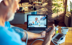 Persona tomándose la presión con un tensiómetro, mientras esta viendo a un doctor en una computadora
